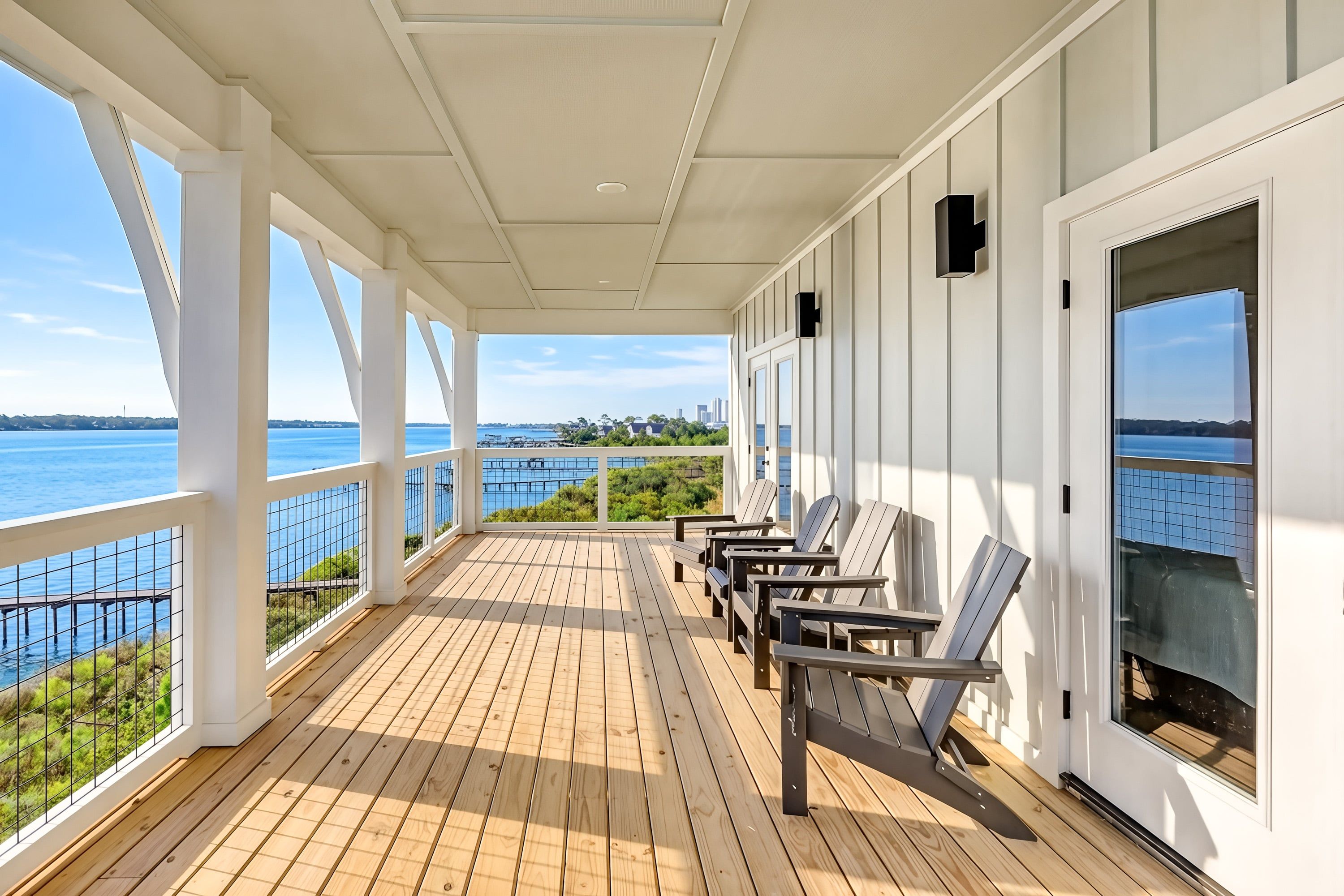 A covered outdoor deck with wooden flooring, white railings, and multiple Adirondack chairs.