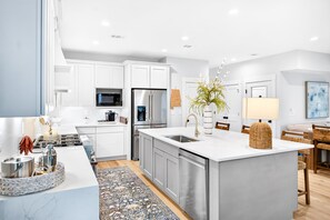 A modern kitchen with white cabinetry, stainless steel appliances, and a central island with a sink. - Laguna Matata by Kaiser | Waterfront Little Lagoon | Heated Pool | Near Beach (Gulf Shores)