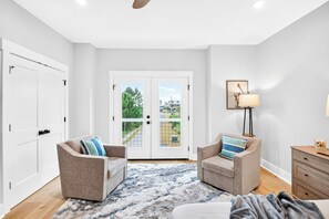 A modern living room with two armchairs, a coffee table, a rug, a lamp, and a view through a glass door. - Laguna Matata by Kaiser | Waterfront Little Lagoon | Heated Pool | Near Beach (Gulf Shores)