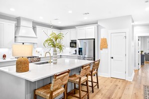 Une cuisine moderne avec des meubles blancs, un grand îlot central doté de tabourets, des appareils en acier inoxydable et une plante en pot.
