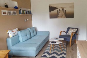 A living room with a light blue sofa, a small round table, a blue armchair, and a painting of a pier on the wall. - Vacation near the Müritz (Klink OT Sembzin)