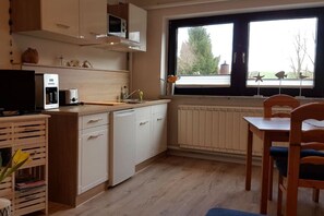 A compact kitchen with a microwave, toaster, and sink. There's a dining table with chairs and a window with a view of trees. - Vacation near the Müritz (Klink OT Sembzin)
