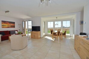 A spacious living area with a sofa, a TV, a dining table with chairs, and a view through large glass doors. - Holiday apartment with 2 bedrooms (Breege)