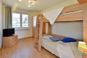 Makuuhuoneessa on kerrossänky, televisio puukehikon päällä, ikkuna, jossa on verhot, ja lamppu sivulla.