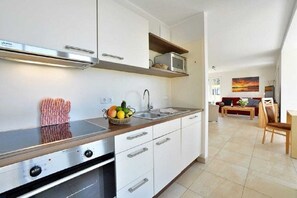 A modern kitchen with a built-in stove, microwave, and sink. There is a dining area with a table and chairs visible in the background. - Holiday apartment with 2 bedrooms (Breege)