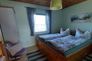 Ein Schlafzimmer mit einem hölzernen Bett, einem Sessel, einem Fenster mit Vorhängen und einem Gemälde an der Wand.
