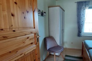 Ein Zimmer mit einem Holzschrank, einer weißen Kommode, einem violetten Sessel und einem Bett.