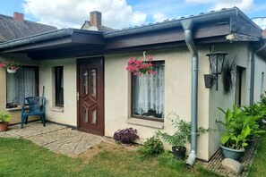 A house with a brown door, a window with a curtain, a blue chair outside, and potted plants. - Bungalow with 2 bedrooms (Großwoltersdorf)