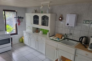 A kitchen with white cabinets, a stove, a sink, and a water heater. - Bungalow with 2 bedrooms (Großwoltersdorf)