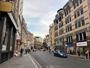Une rue bordée d’immeubles, une voiture bleue et des piétons.