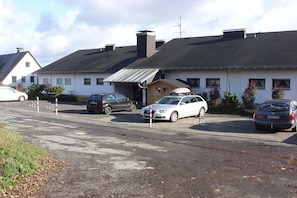Un espace de stationnement où plusieurs voitures sont garées devant un bâtiment doté d’un toit en pente et de nombreuses cheminées.