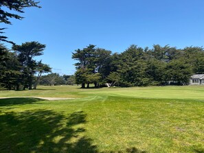 Ein Golfplatz mit blauem Himmel, Bäumen und einem Gebäude im Hintergrund.