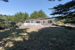 Ein eingeschossiges Holzhaus mit umzäunter Garten, umgeben von dichtem Wald.