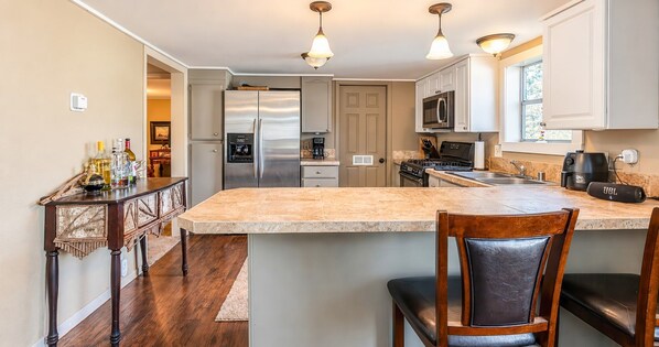 A modern kitchen with a central island, stainless steel appliances, and a bar area. - Corporate Retreat: A Cottage in the City (Auburn Hills)
