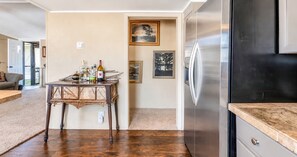 A kitchen with a stainless steel refrigerator, a wooden dining table with various items, and framed pictures on the wall. - Corporate Retreat: A Cottage in the City (Auburn Hills)