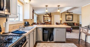 A compact kitchen with a gas stove, a sink, and a small refrigerator. There is a dining area with a table and chairs, and a living room with a sofa and a painting on the wall. - Corporate Retreat: A Cottage in the City (Auburn Hills)