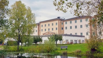 Een hotel met meerdere verdiepingen, een centrale binnenplaats, een vijver en een bankje.