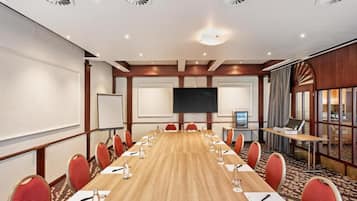 Ein Konferenzraum mit einem langen Tisch, roten Stühlen, einer großen Leinwand und einem Projektor.