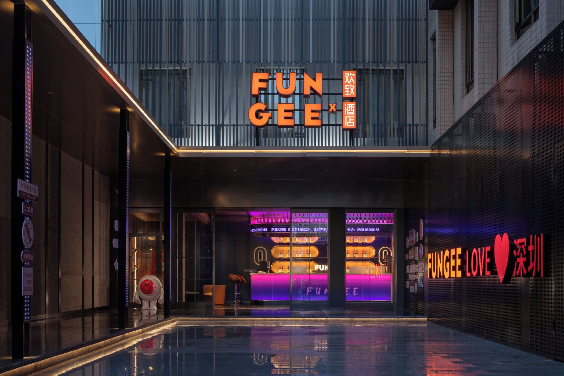 A modern building with a prominent 'FUN GEE' sign, a glass facade, and a reflective pool in front.