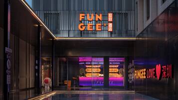 A modern building with a prominent 'FUN GEE' sign, a glass facade, and a reflective pool in front.