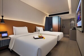 Habitación de hotel con cama, mesita de noche, lámpara y una pantalla digital mostrando información.
