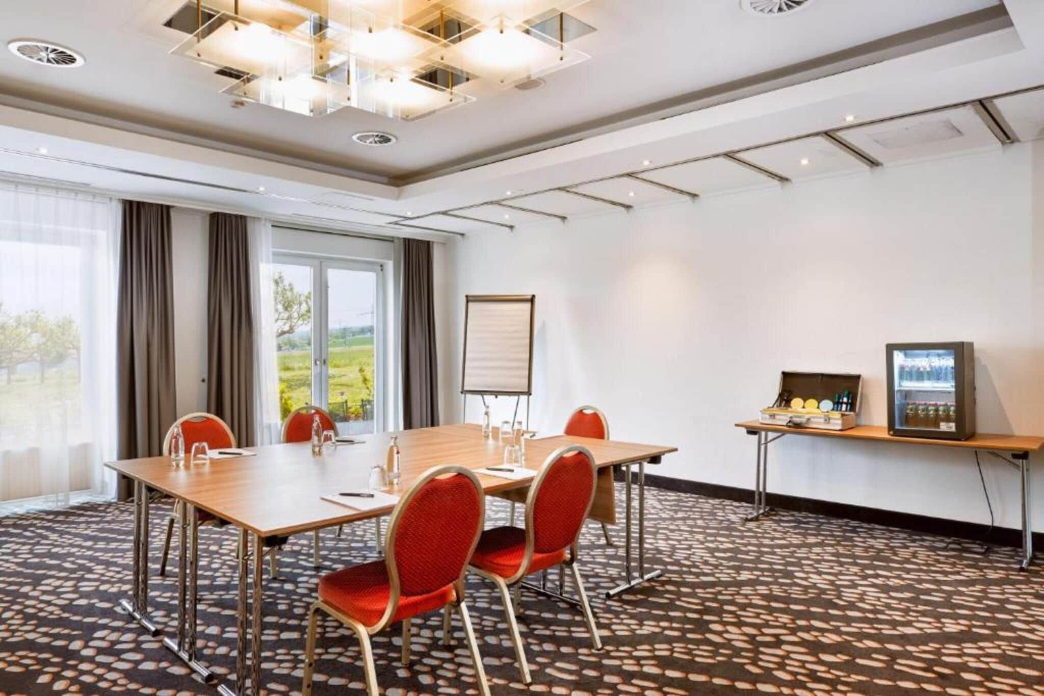 A conference room with a large table, red chairs, a projector screen, and a refrigerator with beverages.