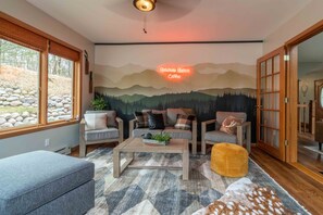 Ein gemütliches Blockhaus-Interieur mit Bergbild, zwei Sofas, einem Couchtisch und einem großen Fenster.