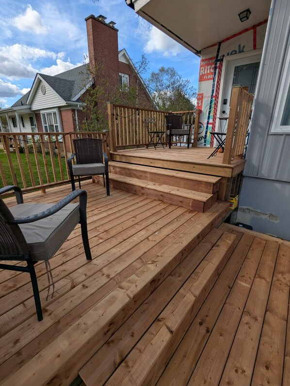 A wooden deck with outdoor furniture, a brick chimney, and a house in the background.