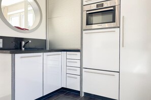 A modern kitchen with white cabinetry, a stainless steel oven, and a black countertop. - Holiday home with 2 bedrooms (Timmendorfer Strand)