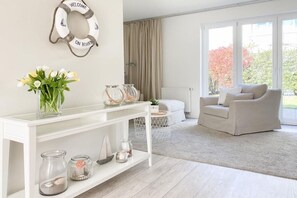 Ein modernes Wohnzimmer mit einer weißen Konsole, einem beigefarbenen Sofa und einem großen Fenster mit Vorhängen.