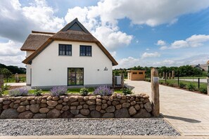 A white house with a thatched roof, a stone wall, and a paved driveway. - Holiday home Seestern (Kramerhof OT Parow)