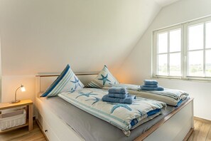 A bedroom with a sloped ceiling, a bed with starfish-themed bedding, a bedside table with a lamp, and a window with a view. - Holiday home Seestern (Kramerhof OT Parow)