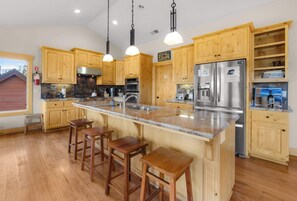 A kitchen with wooden cabinets, a stainless steel refrigerator, and a large island with bar stools. - Shaquinaw - Mountain views, Hot tub & Game Room! (South Lake Tahoe)
