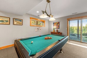 Une table de billard dans une pièce dont un mur est décoré sur le thème de Star Wars, avec une fenêtre et un luminaire au plafond.