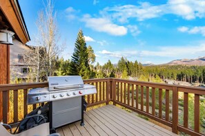 A deck with a barbecue grill, overlooking a forested area with mountains in the distance. - Shaquinaw - Mountain views, Hot tub & Game Room! (South Lake Tahoe)