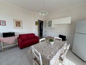 A compact living space with a dining table, a red sofa, a white cabinet, and a microwave on a table. - Holiday house 'Rita's Home' (Paringianu)
