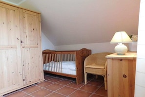 Ein Zimmer mit einem Holzkindbett, einem Korbstuhl und einem Holzschrank.