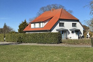 Ett tvåvåningshus med ett rött tak, vita väggar och en veranda med utomhusmöbler.