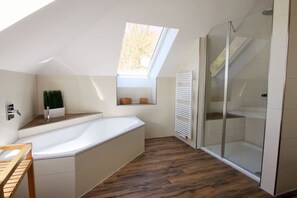 A modern bathroom with a skylight, a bathtub, a shower enclosure, and a wooden floor. - Holiday apartment with 1 bedroom (Ostseebad Sellin)