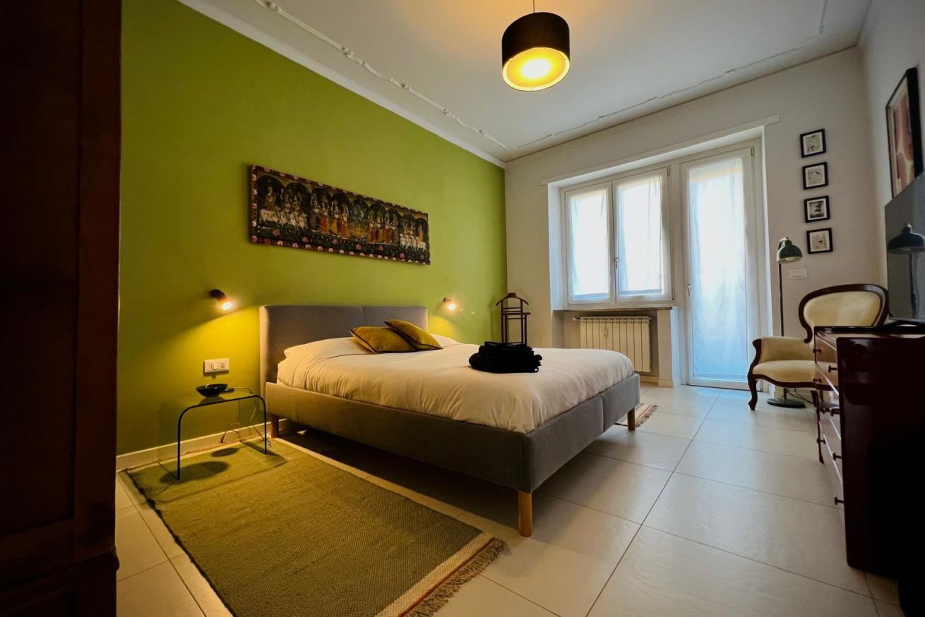 Ein Schlafzimmer mit Bett, Nachttisch, Lampe und einem Fenster mit Vorhängen.
