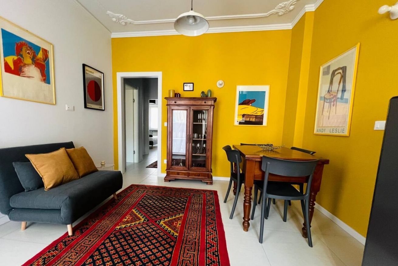 Ein Wohnzimmer mit einer Couch, einem Esstisch mit Stühlen, einem gemusterten Teppich und Bildern an den Wänden.