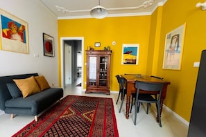 Ein Wohnzimmer mit einer Couch, einem Esstisch mit Stühlen, einem gemusterten Teppich und Bildern an den Wänden.