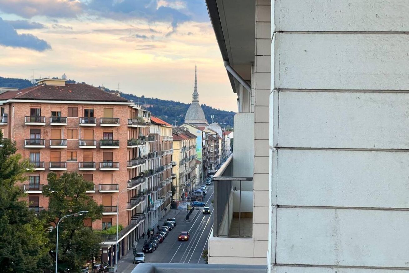 Una strada cittadina con edifici a più piani, un'imponente torre e un cielo sereno.