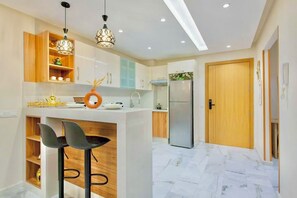 Une cuisine moderne dotée d’un îlot central, de tabourets de bar, de luminaires suspendus et d’un réfrigérateur.