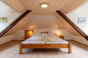 A bedroom with a sloped ceiling, a wooden bed, two bedside tables with lamps, and a small wall-mounted shelf. - Old Forester's Lodge Holiday Apartment Bianca (Bad Peterstal)