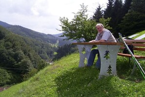Eine Person sitzt auf einer Bank mit Blick auf ein Tal und Hügel im Hintergrund.