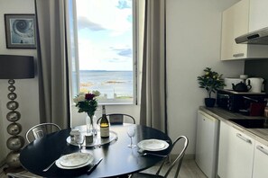 A dining area with a view of the sea, a table set with plates, a wine bottle, and a vase with flowers. - Holiday home in Clohars Carnoët with parking (Clohars Carnoët)
