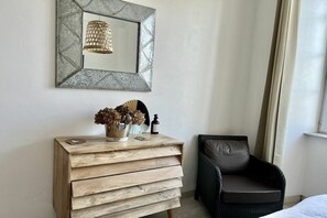 Ein Zimmer mit einem hölzernen Schminktisch, einem Stuhl, einem Spiegel mit geometrischer Rahmen und einer Pendelleuchte.