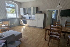 A compact kitchen with a dining area, wooden flooring, and a television. - Old School Ahrensberg (Ahrensberg)