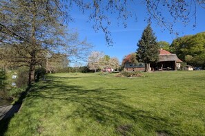 A grassy area with a pond, trees, and a building with a red roof. - Old School Ahrensberg (Ahrensberg)